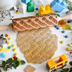 Peut inclure: Un rouleau à pâtisserie en bois avec le nom "Oliver" gravé dessus. Le rouleau à pâtisserie est sur une surface blanche avec un morceau de pâte qui a été roulé avec le rouleau. La pâte est imprimée avec le nom "Oliver".