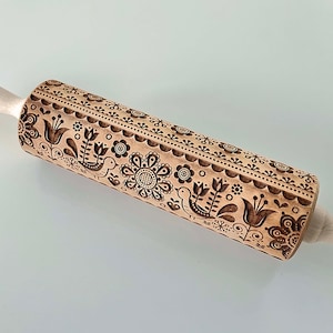 Può includere: Mattarello in legno con un intricato disegno intagliato di fiori e uccelli. Il motivo è ripetuto lungo la superficie del mattarello, con manici in legno chiaro. Il design include fiori, uccelli e bordi decorativi.