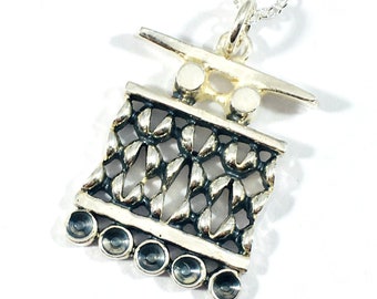 May include: A silver necklace with a detailed pendant featuring a geometric design with a woven pattern. The pendant has a silver chain and a silver clasp.