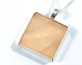 May include: A silver chain necklace with a square pendant featuring a light pink stone.