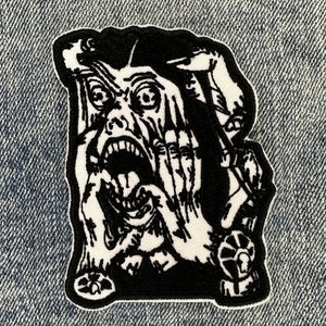 May include: Black and white embroidered patch of a screaming face with hands covering the face. The face is contorted in a scream with the mouth wide open and the eyes wide with fear.