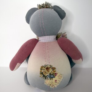 May include: A gray and pink patchwork teddy bear with a striped neck scarf and a floral patch on its back.