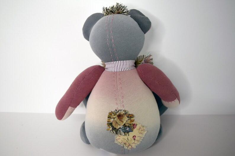 May include: A gray and pink patchwork teddy bear with a striped neck scarf and a floral patch on its back.
