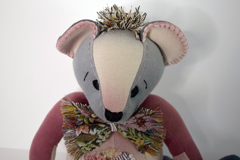 May include: A handmade plush toy bear with gray and pink fabric, a black nose, and a brown and green patterned bow tie.