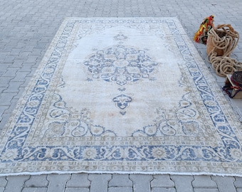 May include: A vintage rug with a cream background and a blue and cream floral pattern. The rug has a frayed edge.