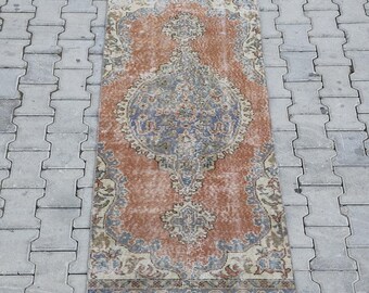 Op de afbeelding: Een rechthoekig, versleten tapijt met een centraal medaillonontwerp. Het tapijt heeft een warm kleurenpalet van oranje, blauw en crème, met ingewikkelde bloempatronen. Het tapijt meet ongeveer 60 x 120 cm.