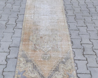 May include: A vintage runner rug with a faded, light brown background and a geometric pattern in shades of blue, brown, and beige. The rug has a distressed, worn look, giving it a rustic and charming appeal.