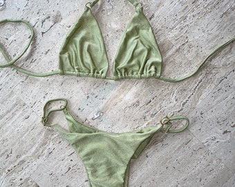 Puede incluir: Un top y una parte inferior de bikini verde con anillos dorados. El bikini está hecho de una tela brillante.
