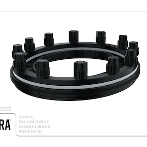 Könnte beinhalten: Ein schwarzer 3D-gedruckter Ring mit 12 Knöpfen am Umfang. Der Ring ist aus nachhaltigem Material gefertigt und zu 100% biologisch abbaubar. Der Text "RA" ist auf den Ring gedruckt. Der Text "3D PRINTED 100% BIODEGRADABLE SUSTAINABLE MATERIAL MADE IN THE USA" ist unter dem Ring gedruckt.