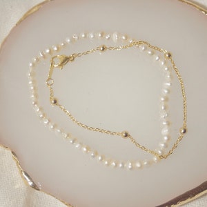 May include: A delicate gold chain bracelet with small pearl accents. The bracelet is layered with a second strand of pearls, creating a simple and elegant look.