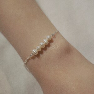 以下が含まれることがあります： 白い真珠が並んだ、繊細なシルバーチェーンのブレスレットです。