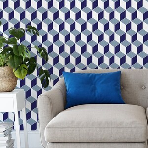 May include: A light gray couch with a blue throw pillow in front of a wall with a geometric pattern of blue and gray cubes.