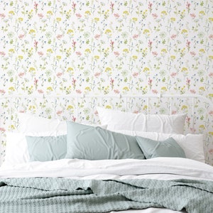 May include: A white bed with a white metal headboard and a light blue blanket. The wall behind the bed is covered in a white wallpaper with a delicate floral pattern in shades of pink, yellow, and blue.