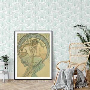 A room with art deco wallpaper behind a wicker chair and a plant and a large framed art nouveau portrait.