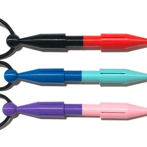 Può includere: Tre strumenti appuntiti retrattili di diversi colori con cordini neri attaccati. Gli strumenti sono nero e rosso, blu e turchese, e viola e rosa.