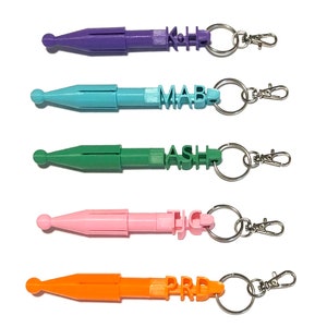 May include: Five colorful keychain tools with a pointed tip and a retractable design. Each keychain has a different name spelled out in block letters: KJH, MAB, ASH, TJC, and PRD.