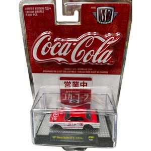 May include: A red and white 1971 Nissan Skyline GT-R die-cast model car in a clear display case. The packaging features the Coca-Cola logo and Japanese text. Limited edition, scale 1:64.