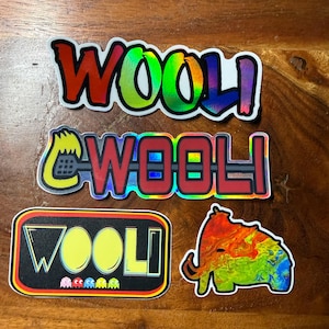 以下が含まれることがあります： WOOLIという文字がデザインされた4枚のステッカー。1枚はホログラフィックな虹色のグラデーション、もう1枚はWOOLIの文字と黄色いキャラクター、長方形のステッカーにはWOOLIの文字と小さなゴースト、そしてマンモスの形をしたステッカーが含まれています。
