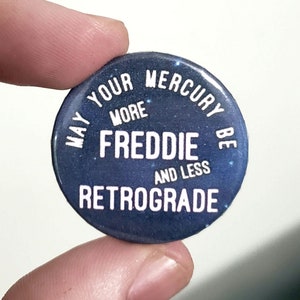 Peut inclure: Un bouton bleu avec du texte blanc qui dit "Que votre Mercure soit plus Freddie et moins rétrograde".