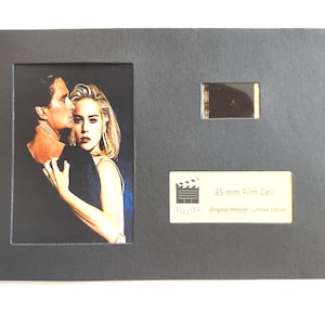 May include: A framed 35mm film cell featuring a movie still of a man and woman embracing. The frame is dark gray with a rectangular opening for the image and a smaller opening for the film cell. Text on the frame reads "35 mm Film Cell".