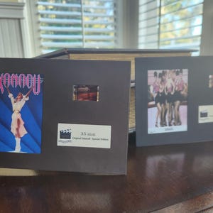 May include: Two framed film cells, one with the word "Xanadu" and a figure, the other with a group of women. Both include film strips and text indicating "35 mm Original Movie Special Edition".