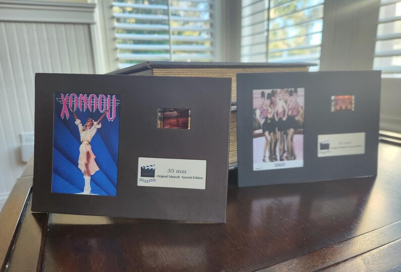 May include: Two framed film cells, one with the word "Xanadu" and a figure, the other with a group of women. Both include film strips and text indicating "35 mm Original Movie Special Edition".