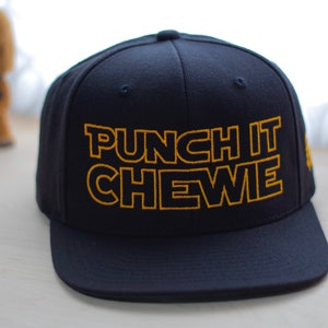 Könnte beinhalten: Eine marineblaue Baseballkappe mit einem gelben gestickten Design, das "Punch It Chewie" lautet.