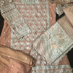 May include: A light brown dress with silver embroidery and embellishments. The dress has a long sleeve and a matching dupatta.