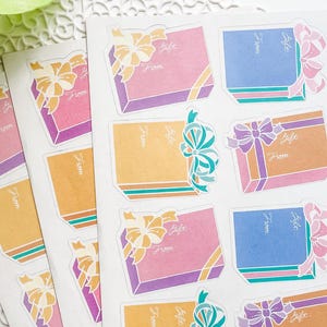 May include: Sheets of gift stickers with colorful gift box designs. Each sticker features a box with a bow and the words "Gift" and "From". The boxes are in shades of pink, blue, and orange with purple and teal accents.