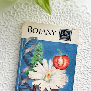 May include: A vintage paperback book titled Botany, A Golden Science Guide. The cover features a blue background with illustrations of a DNA double helix, a white daisy, a halved red cherry, a green tree, and roots with small red berries.
