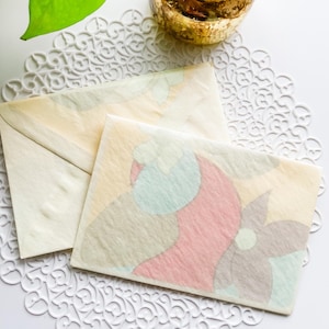 May include: Two vintage envelopes with a floral design. The envelopes are cream colored with a light pink, blue, and yellow floral pattern. The envelopes are on a white doily.