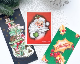 May include: Three vintage Christmas cards. One card features a stack of presents in a sleigh with the text "Best Wishes". Another card features Santa Claus reading a book with the text "Greetings". The third card features a holly sprig with red berries and the text "At Christmas".