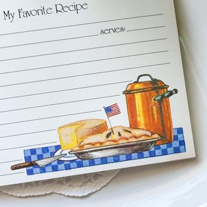 May include: A recipe card with the text "My Favorite Recipe" at the top. The card features illustrations of a pie, cheese, a copper pot, and an American flag. The card is on a white plate.