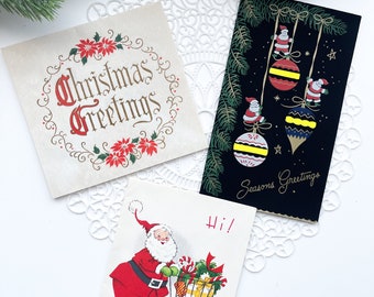 May include: Three vintage Christmas cards. One card features a red poinsettia with the text "Christmas Greetings". Another card features a black background with three gold and red ornaments with the text "Seasons Greetings". The third card features a cartoon Santa Claus with a shopping cart full of presents and the text "Hi!"