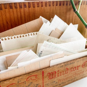 May include: A wooden box filled with a variety of vintage paper ephemera. The papers include lined, graph, and blank sheets in various sizes and shades of cream and tan. The box has dovetail joints and red text that reads "Windsor Cheese".