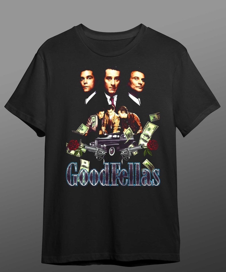 Pu&ograve; includere: Una maglietta nera con una grafica di tre uomini del film Quei bravi ragazzi. Gli uomini sono in piedi davanti a un'auto con soldi e pistole intorno a loro. Il testo "Goodfellas" &egrave; stampato in lettere blu e bianche sotto la grafica.