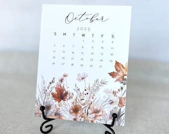 May include: A white card with a black calendar for October 2025. The calendar has a floral design with fall colors, including orange, brown, and beige.