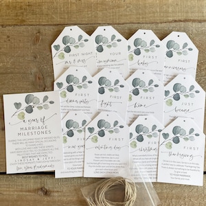 May include: A set of 10 watercolor-style gift tags with eucalyptus leaves and a white background. Each tag features a different milestone for a first year of marriage, such as "First Night", "First Fight", "First Christmas", and "First Thanksgiving".