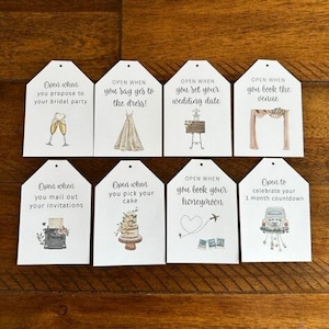 May include: Eight white tags with brown text and illustrations. Each tag has a different wedding milestone with text such as "Open when you propose to your bridal party" and "Open when you book your honeymoon".