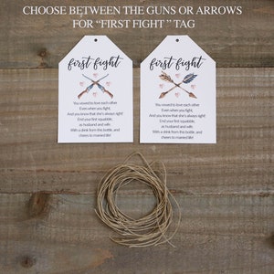 May include: Two white tags with the text "first fight" printed in pink. The tags feature a watercolour illustration of either guns or arrows crossed with hearts. The text on the tags reads: "You vowed to love each other Even when you fight, And you know that she's always right! End your first squabble, as husband and wife With a drink from this bottle, and cheers to married life!"