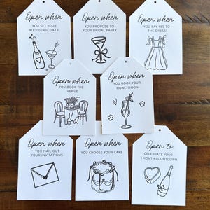 May include: Set of ten white wedding favor tags with black ink. Each tag has a different illustration and the text "Open when" or "Open to" followed by a wedding-related event.