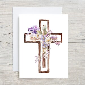 May include: A watercolour illustration of a wooden cross adorned with purple and white flowers. The cross is a simple design with a rustic look.