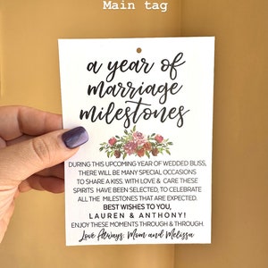 May include: A white card with a floral design and the text "a year of marriage milestones". The card also includes the text "During this upcoming year of wedded bliss, there will be many special occasions to share a kiss. With love & care these spirits have been selected, to celebrate all the milestones that are expected. Best wishes to you, Lauren & Anthony! Enjoy these moments through & through. Love Always. Mom and Melissa"