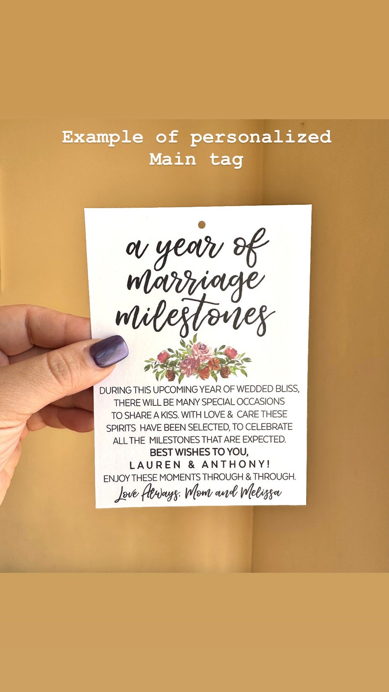 May include: A white card with a floral design and the text "a year of marriage milestones". The card also includes the text "During this upcoming year of wedded bliss, there will be many special occasions to share a kiss. With love & care these spirits have been selected, to celebrate all the milestones that are expected. Best wishes to you, Lauren & Anthony! Enjoy these moments through & through. Love Always. Mom and Melissa"