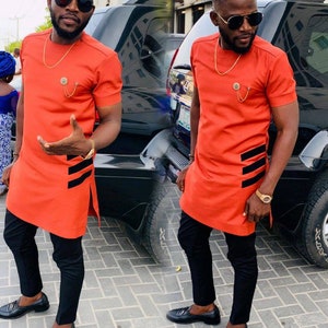 May include: An orange short-sleeved shirt with black stripes and black pants. The shirt has a gold chain and a decorative pin. The outfit is paired with black loafers and sunglasses. The image is a split image.