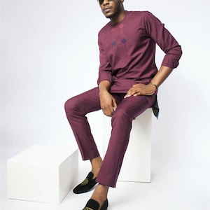 May include: A maroon long-sleeved shirt with embroidered details and matching pants. The person is wearing black loafers with gold embroidery.