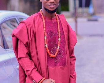 May include: A man wearing a red and burgundy traditional African outfit with a red hat, beaded necklace, and a walking stick.