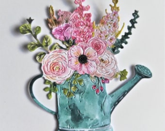 以下が含まれることがあります： ピンク、白、緑の花のフラワーアレンジメントが施された、ターコイズブルーのじょうろ。花はじょうろにアレンジされており、茎は上部から突き出ています。