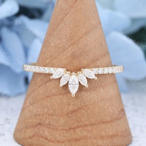 May include: A delicate gold ring featuring a marquise-shaped diamond centre stone and smaller diamonds set in a curved band. The ring is displayed on a wooden ring holder.