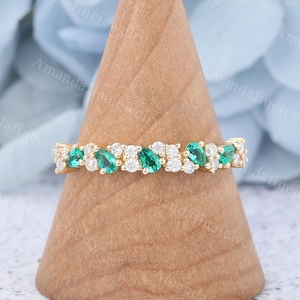Puede incluir: Un delicado anillo de banda de oro con una fila de piedras preciosas en forma de pera de color verde esmeralda y diamantes redondos más pequeños.